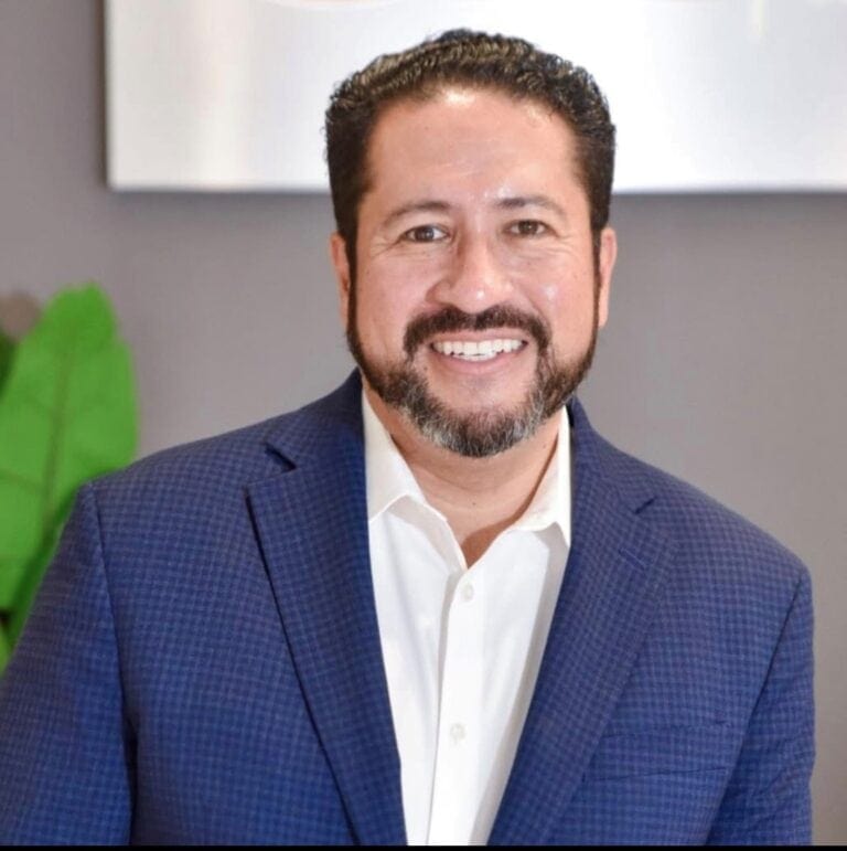 Rick Ruiz smiling in a blue suit, team photo for real estate services.